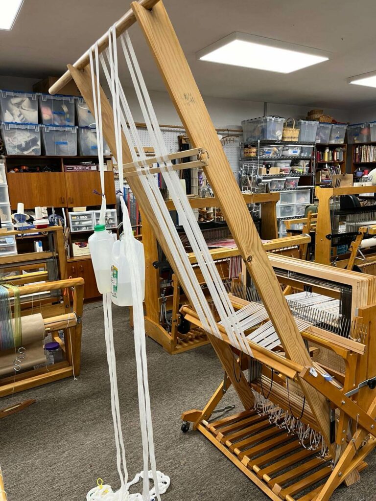 Jugs hand from the warp, approximately halfway between the floor and the dowel, as the warp is wound on
